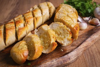 Garlic bread, baguette with garlic butter and herbs, on a wooden board, with herbs and garlic