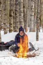 A woman warms herself by a campfire in winter, Gaspesie national park, Province of Quebec, Canada,