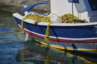 A blue fishing boat with a fishing net lies on the water in the harbour, Analipsi, Maltezana,