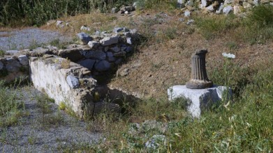 An old wall and a column surrounded by grass and flowers, ancient Roman bath, Tallaras, Analipsi,