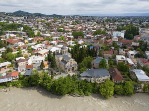 Close-up of a city view with a central church, residential houses and a river next to wooded hills,