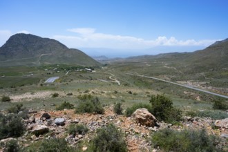Wide landscape with hills and a winding road under a blue sky, view from the Tukh Manuk Pass to the