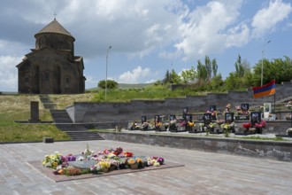 Church with cemetery in the foreground, decorated with flowers and Armenian flag under a cloudy