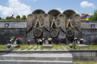 Stone monument with figures of angels and flowers, framed by an Armenian flag, cemetery, Sisian,