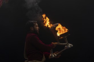 Hindu priest performing the Aarti ritual, holding a burning oil lamp, at the Ganges, Bangali Tola,