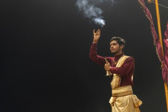 Hindu priest performing the Aarti ritual, at the Ganges, holding incense sticks and a bell, Bangali
