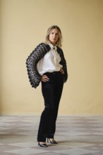 A middle-aged woman stands with hands on her hips in a trendy outfit featuring a unique sweater and