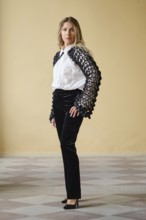 Brightly lit indoor location displays a middle-aged fashion model standing confidently. She wears a