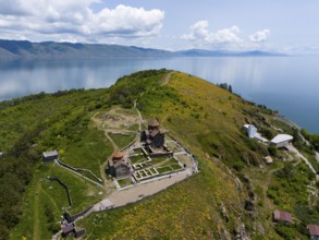 Panorama of a monastery on a green hill with a view of a lake and mountains under a cloudy sky,