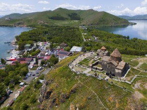 Aerial view of a busy monastery on a hill surrounded by a lake, mountains and a small village,