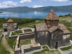 Historic stone monastery with a lake and mountain panorama under a cloudy sky, aerial view,