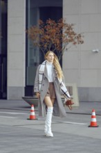 A tall model walks down a modern city street, showcasing chic winter fashion with a stylish