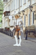 A young woman dressed in a fashionable autumn outfit stopped on a cobblestone street and is looking