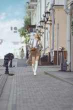 A young woman walks confidently down a cobblestone street wearing a stylish trench coat and