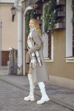 A woman with long blonde hair strolls confidently down a cobblestone street, wearing a stylish