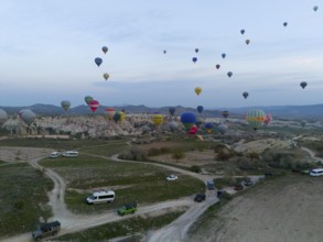 Balloons rise into the sky while vehicles stand on the ground in an open landscape, aerial view,