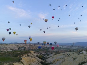 Numerous balloons in bright colours float over a hilly, natural landscape, aerial view, Göreme