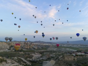 Many colourful hot air balloons float over a vast Turkish landscape in the early morning, aerial