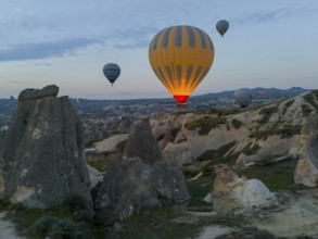 Hot air balloons hovering over a rocky landscape at dawn in Cappadocia, aerial view, Göreme