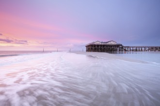 Pile dwellings in St. Peter-Ording in front of the surf in the bright red evening light by the sea