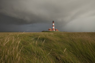 Illuminated Westerheversand lighthouse on the North Sea under dark storm clouds
