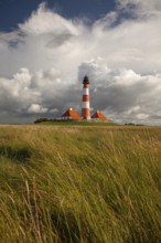 Illuminated Westerheversand lighthouse on the North Sea under dark storm clouds