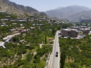 Village with a road winding through a mountainous landscape with green vegetation, aerial view,