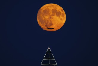 The full moon passes over the top of the Messeturm in Frankfurt am Main, while the silhouette of an