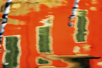 Colourful façade detail reflected in the water of a canal, Burano, Venice, Veneto, Italy