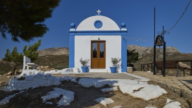 White chapel with blue façade and cross in a mountainous setting under a clear sky, Panagia tou