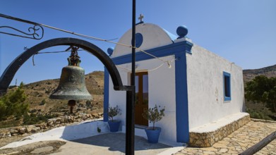 Small white-blue chapel in the countryside with bell in the foreground and blue sky in the