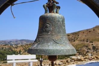 Antique metal bell in rural setting with background landscape and blue sky, Panagia tou