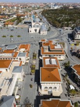 Bird's eye view of an urban landscape with red roofs and a mosque in the background in sunny