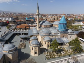 Historic mosque with minaret and domes in the middle of a cityscape under a blue sky, aerial view,