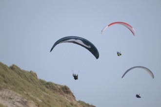 Three paragliders or paragliders in front of a blue sky over a dune landscape, near Hvide Sande,