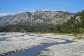 A calm river flows through a wide gravel bed, framed by forested mountains, Dargaz River near