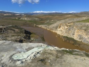 Vast landscape with brown river and rocky gorge under blue sky and white clouds, aerial view,