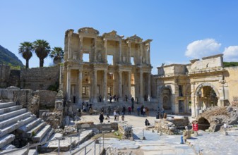 Ancient ruins with imposing columned facades and palm trees, surrounded by visitors under a blue