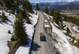 Car on winding mountain road, surrounded by snow and fir trees, with wide view, aerial view,