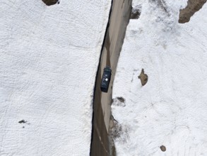 Aerial view of a car driving on a narrow snowy road between high snow walls, aerial view, camper,