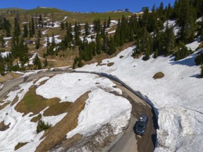 A winding road leads through a landscape of snow-covered hills and pine trees under a clear blue