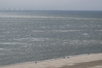 Wide sea view with sandy beach and pedestrians, wind turbines on the horizon, North Sea, Denmark