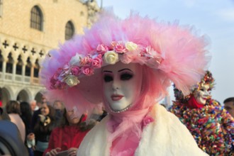Venetian mask, disguised woman with big pink hat, walker, crowd on St Mark's Square, Carnival in