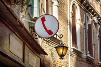 Sign with pictogram, red telephone receiver, public telephone, facade of a restaurant with street