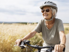 An elderly lady, a senior citizen with a bicycle helmet, rides a bicycle and smiles in a friendly