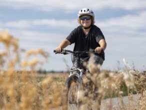 A boy with a bicycle helmet rides a bicycle and smiles friendly into the camera, AI generated, AI