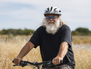 A man, senior citizen with a bicycle helmet rides on a bicycle and smiles friendly into the camera,