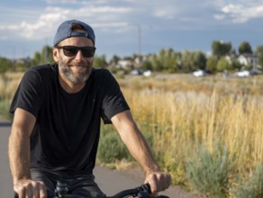 A middle-aged man rides a bicycle and smiles friendly into the camera, AI generated, AI generated