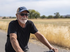 A man, senior citizen rides a bicycle and smiles friendly into the camera, AI generated, AI