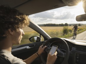A car driver is dazzled by the sun and looks at his smartphone while driving, putting himself, the